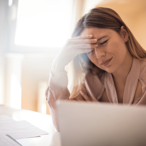 Woman experiencing migraine pain while using a laptop, illustrating the impact of migraines on daily activities and the need for effective IV treatment options.